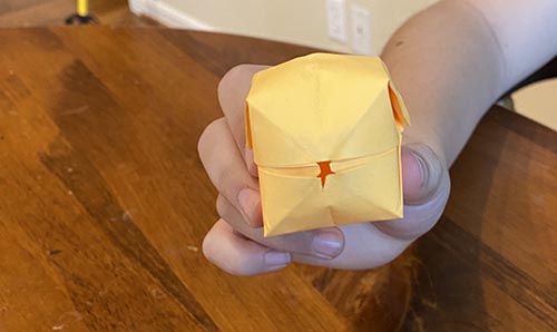 A person showcasing a yellow origami bird on a table.