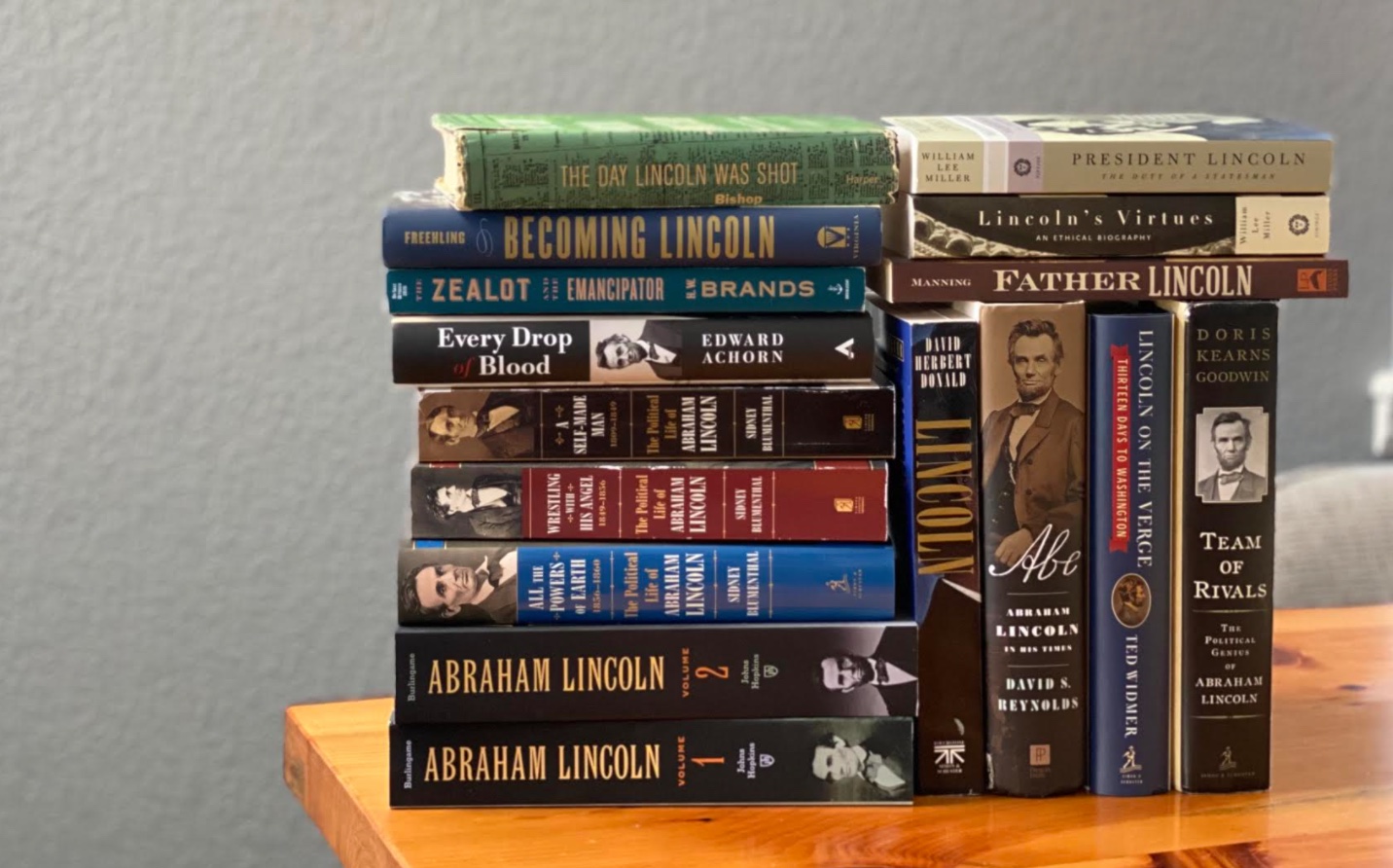 A stack of biography books on a wooden table.