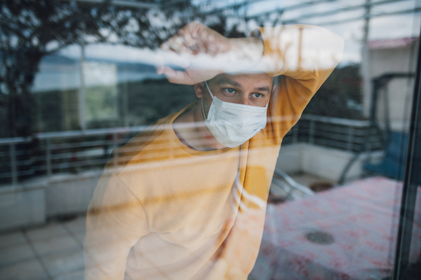 A man wearing a medical mask looks out of a window during a crisis.