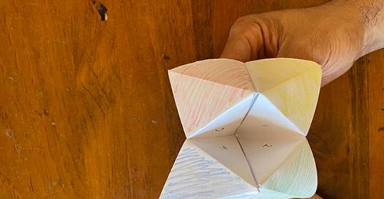 A person holding a paper toy on a wooden table.