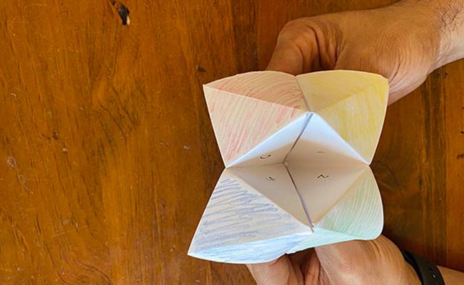 A person holding a paper toy on a wooden table.