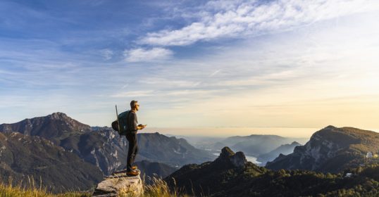 A man with outdoor competence standing on top of a mountain admiring the view.