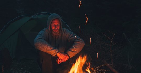 A man reflecting by a campfire.