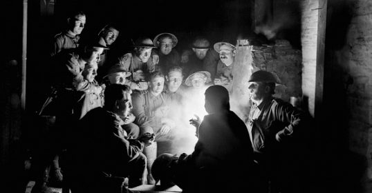 A group of people sitting around a fire while recording a podcast in a dark room.
