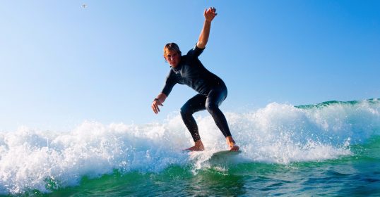 A man in a wetsuit gracefully rides a wave on a surfboard, embodying the thrill of learning new skills.