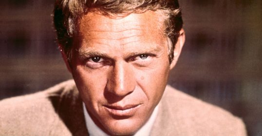 A man in a tan suit is exuding coolness as he stares at the camera.