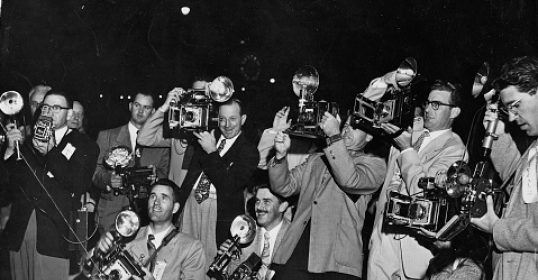 A group of men holding cameras at a party, reminiscent of Alexander the Great.