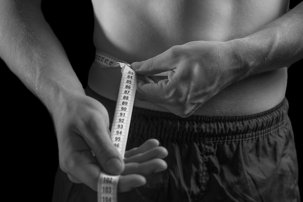 A man is measuring his waist with a measuring tape to track his body fat.