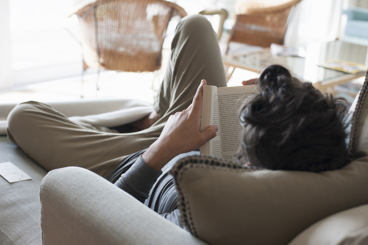 A man reading a book on the couch.