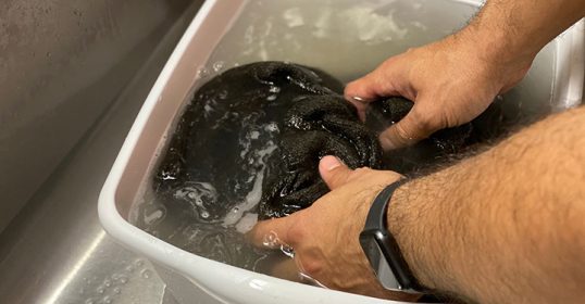 A person washing a black towel in a sink.
