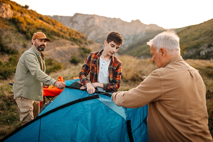 A father is setting up a tent in the mountains, initiating his family into the beauty of nature.