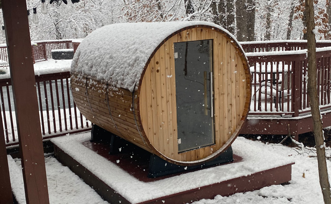 A wooden sauna covered in snow on a deck creates a peaceful retreat for the mind.