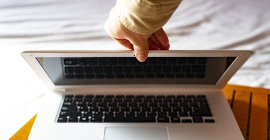 A person holding a laptop on a bed while checking emails.