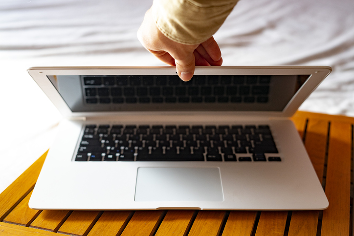 A person holding a laptop on a bed while checking emails.