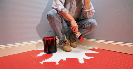 A man painting a room with red paint while listening to a podcast.