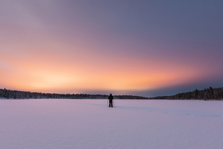 A person showcasing Sisu stands on a snow covered field at sunset.