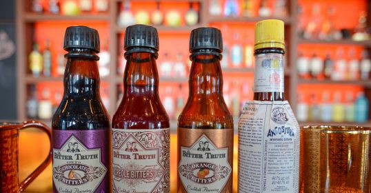 Three bottles of bitters are lined up on a bar.