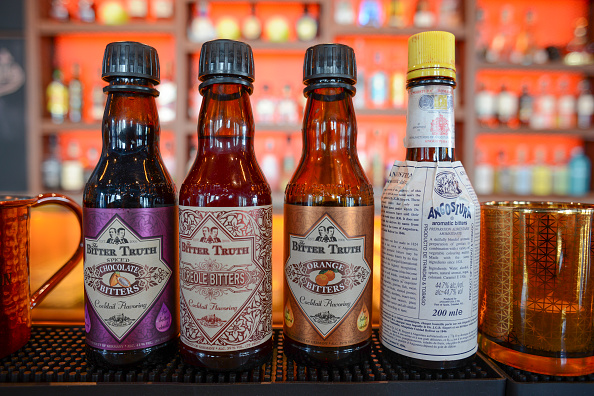 Three bottles of bitters are lined up on a bar.