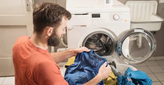 A man is simplifying his laundry routine by putting clothes into a washing machine.