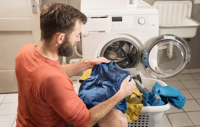 A man is simplifying his laundry routine by putting clothes into a washing machine.
