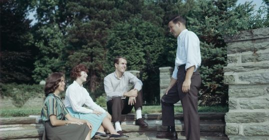 Four people sitting on steps in front of a building.