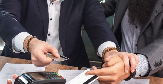 A group of businessmen are graciously paying their restaurant tab with a credit card.