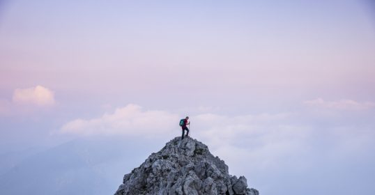 A person standing on top of a mountain, reflecting on how to overcome the Comfort Crisis.