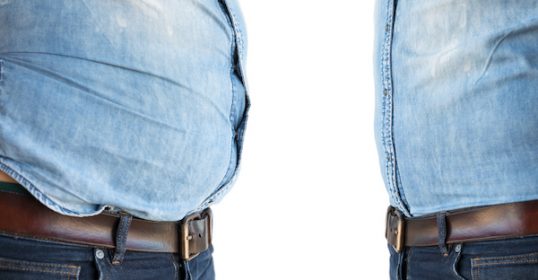 A man wearing a denim shirt with a belt walks confidently down the street.