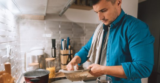 A man in a blue shirt is cooking in the kitchen.