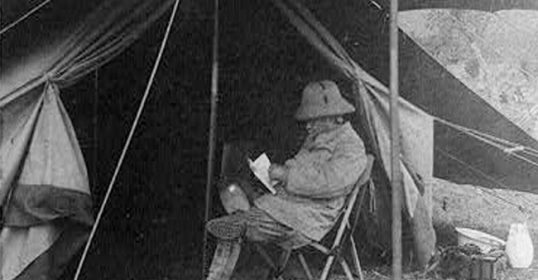 A man in a tent enjoying some vacation reading.