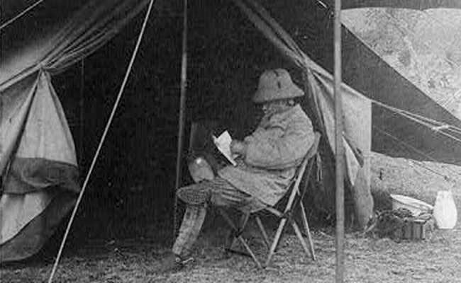 A man in a tent enjoying some vacation reading.