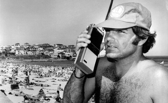 An introduction of a man in a hat using a walkie talkie on the beach.