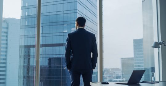 A businessman in a suit standing in front of a window, wanting to record a podcast.