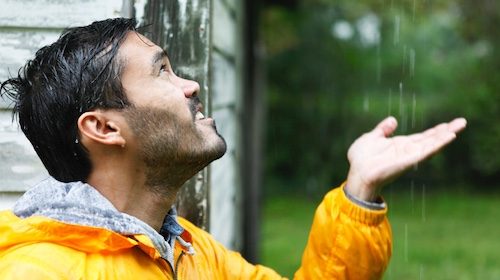 A man in a yellow jacket is looking up at the rain, predicting the weather.