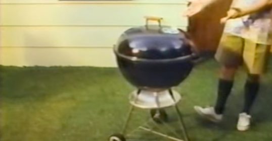 A man standing next to a classic Weber Kettle Grill.