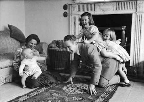 A wholesome black and white photo of a family playing on a rug.