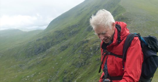 A man in a red jacket standing on top of a mountain.
