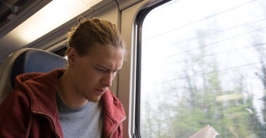 A man immersed in a book while on a train, gaining knowledge about the modern world.