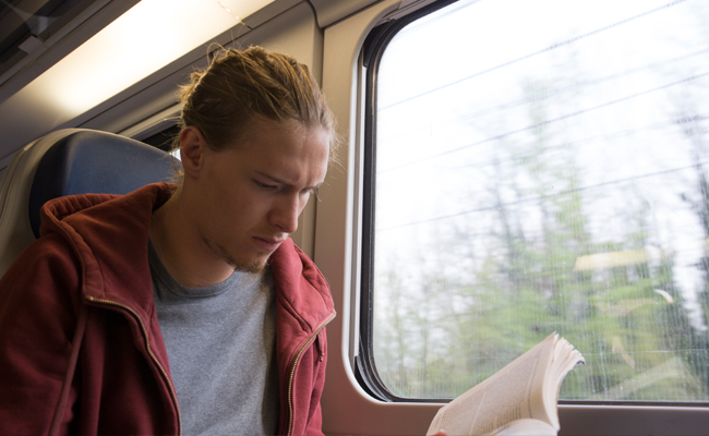 A man immersed in a book while on a train, gaining knowledge about the modern world.