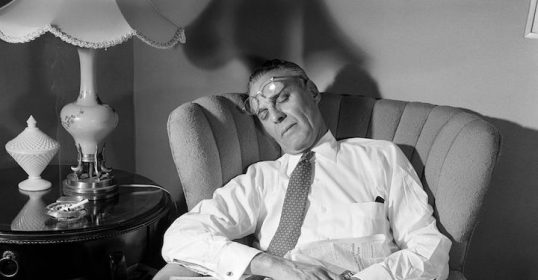 A man sitting in a chair reading a newspaper by Erich Fromm.