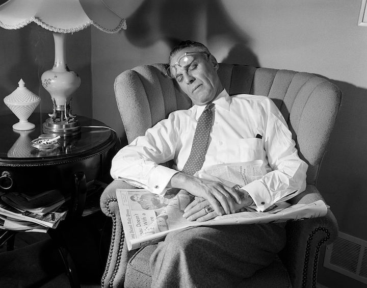 A man sitting in a chair reading a newspaper by Erich Fromm.