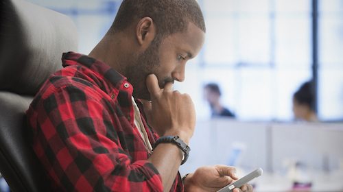 A man sitting in an office chair texting on his cell phone.