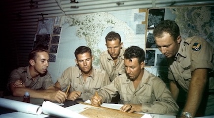 A group of men in military uniforms strategizing around a map.