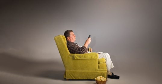 A dad sitting in a chair and using a cell phone.