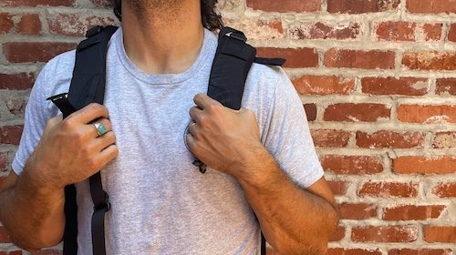 A man with the best backpack stands in front of a brick wall.