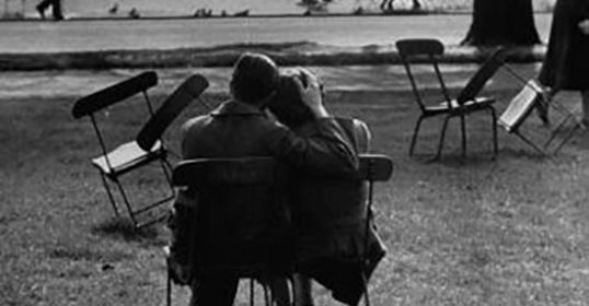 A black and white photo of a man and woman sitting on chairs in a park.