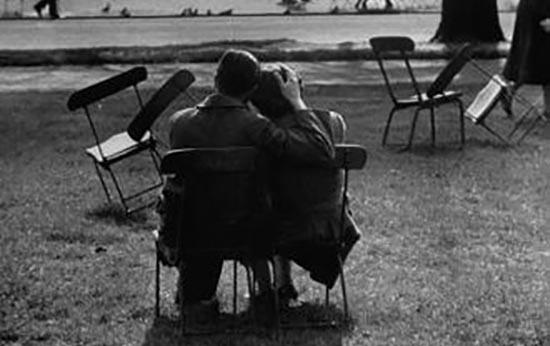 A black and white photo of a man and woman sitting on chairs in a park.