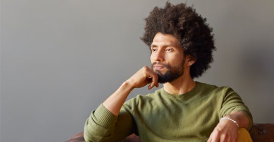 A man with afro hair sitting on a leather couch, in introspection.