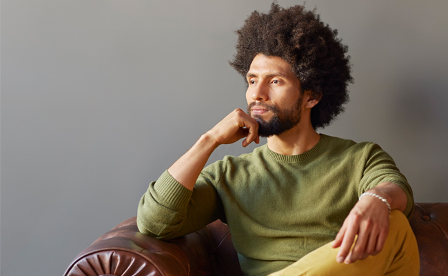 A man with afro hair sitting on a leather couch, in introspection.