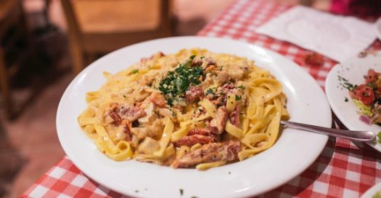 A plate of pasta on a table with a checkered tablecloth is laid out.